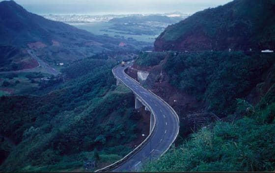 An aerial view of the highway to the windward side of O'ahu on the way to the North Shore, with Kane'ohe and the blue Pacific Ocean beyond.