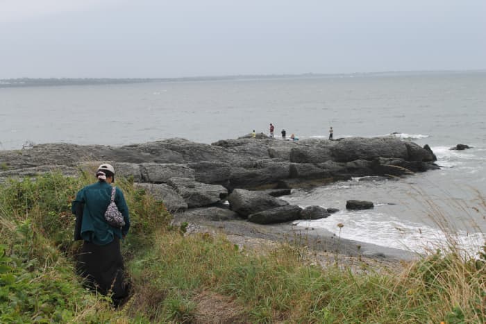 The end of the Cliff Walk trails off into...literally trails. In the distance you can see rocks you can walk on. The woman in the photo is walking along a part of the Cliff Walk. The end of the walk is off photo, behind the woman.