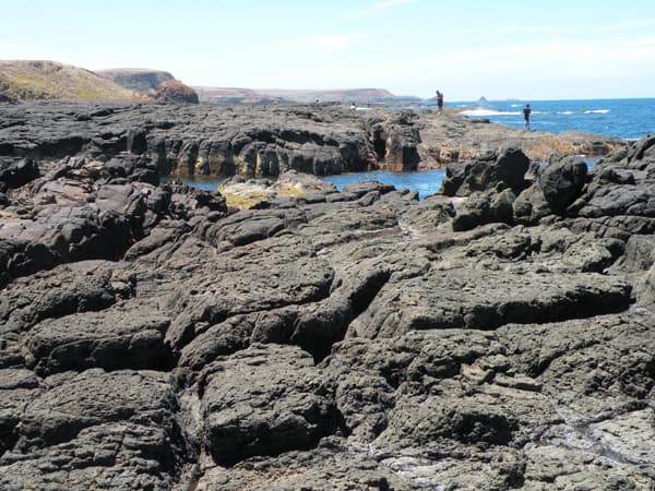 Fishermen standing on the top of the interesting columnar jointed basalt display. Photo taken facing Watt Point from Kennon Head.