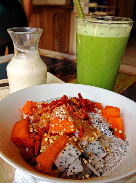 Cereal bowl of tropical fruits, goji berries, chia seeds, with vegan yogurt and green veggie juice.