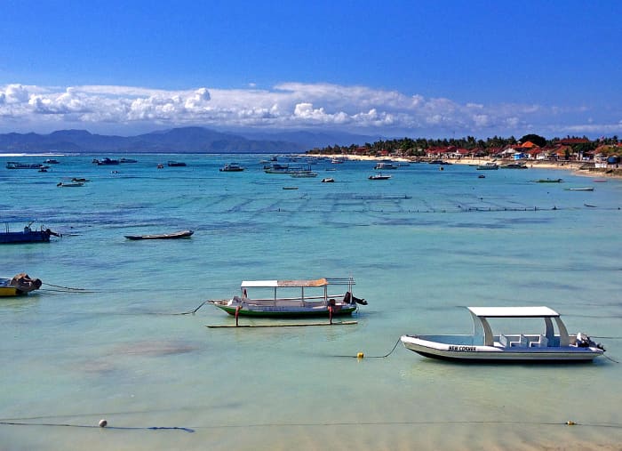 Calm blue water off the beachfront. Mainland Bali can be seen in the horizon with clouds.