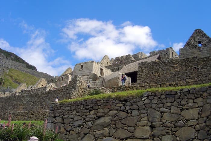 Looking upward past the masterfully constructed stone walls of Machu Picchu to the brilliant blue sky adorned by a few clouds.
