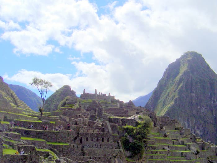A side view of Machu Picchu with tourists walking along the terraces and rock walls; the scene is enhanced by the stunning sky.
