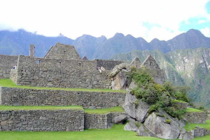 View of a young couple relaxing and enjoying the serenity of Machu Picchu's walls and terraces after a day of touring. The Andes are in the background.