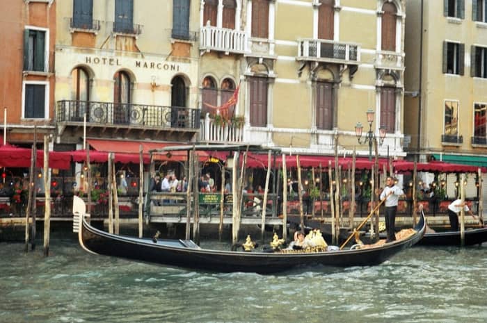 An elegant, classic gondola being propelled through the Grand Canal in front of the Hotel Marconi in central Venice.