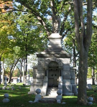 Photograph of the Hackley family monument, a large granite mausoleum with an arched and recessed entryway and an angel on top. The steps leading up to the entry are flanked by large granite spheres. Larger spheres mark the plot corners.