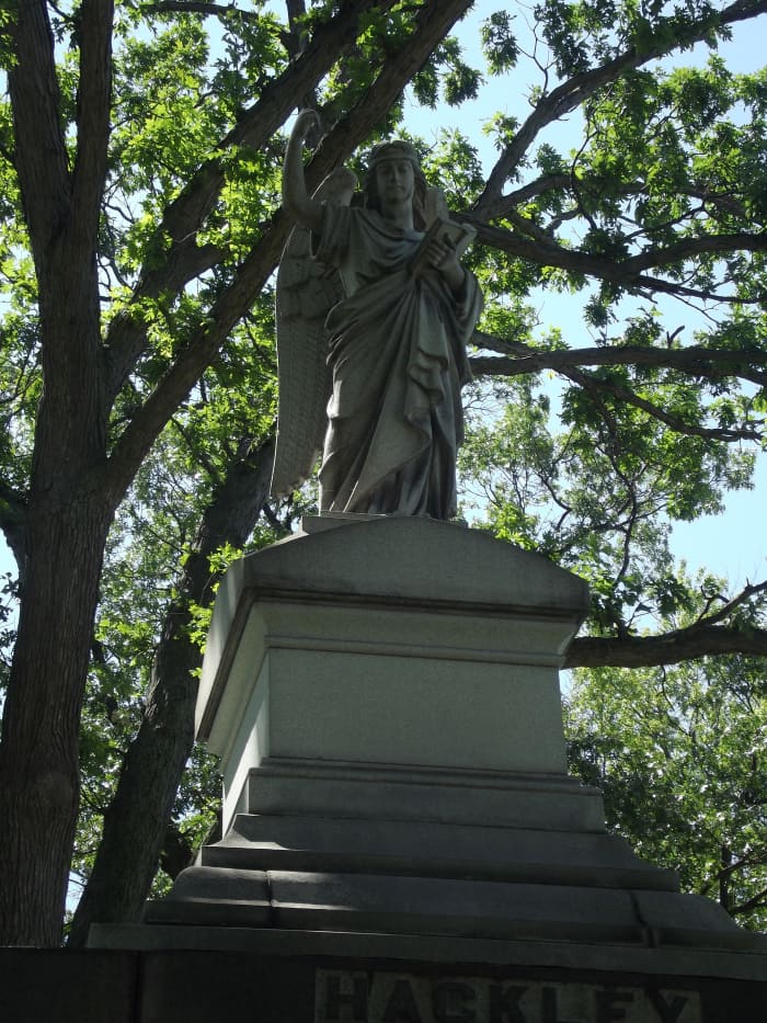 The angel at the top of the Hackley monument. The angel has its wings folded back and is pointing upward while the other holds a book close to the angel's body. Evergreen Cemetery, Muskegon, MI.