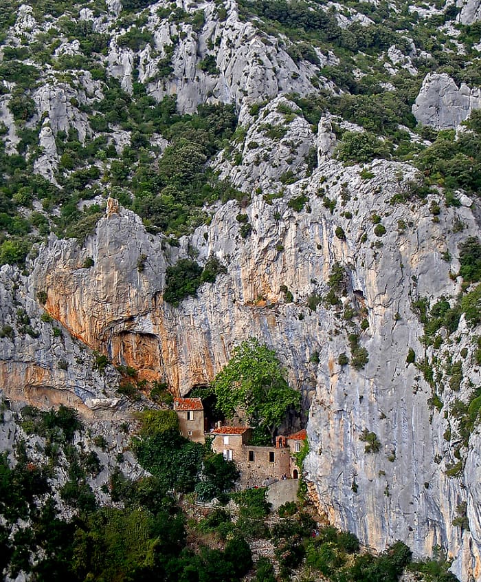 Ermitage de Galamus perches on a vertical rock cliff. "Ermitage" means hermitage which is related to hermit - someone who retreats from society to live in solitude, often for religious reasons.