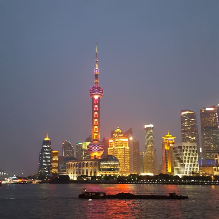 A boat glides along the HuangPu river in front of the Lujiazui finance district skyscrapers. The tall tower with the two spheres is the Oriental Pearl Tower. Visit the Bund at night to see the lit towers changing colors.