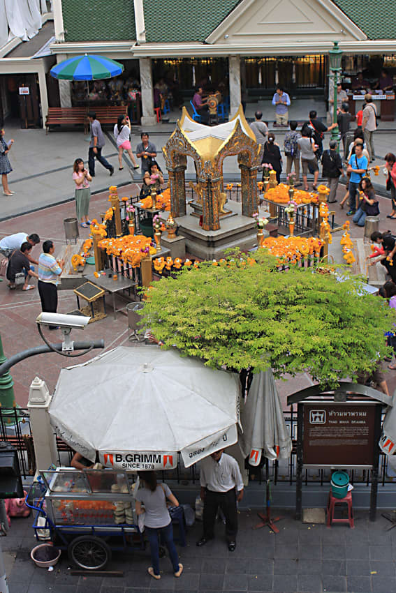 The shrine in the forecourt of the Grand Erawan Hotel, with street vendors in the foreground and the hotel entrance behind