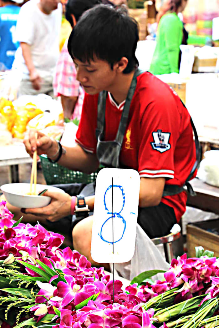 A flower seller pauses to enjoy lunch. The flowers are that most traditional of Thailand blooms - pink-purple orchids