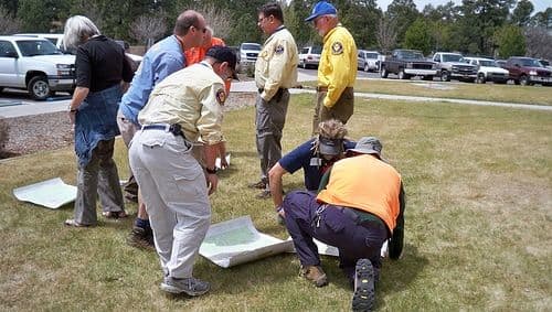 Land navigation with the sun. Here, you see the students orienting their maps to due south, then placing pens on the map to determine direction of travel to their desired destinations.