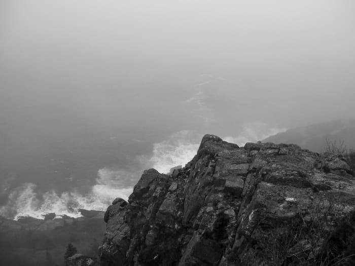 A section of Newfoundland's rugged coastline shrouded in fog. Waves pound the rocky shore far below.