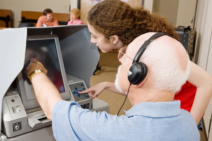 A poll worker shows a voter how to use an accessible voting machine. Image © Can Stock Photo Inc. / lisafx.