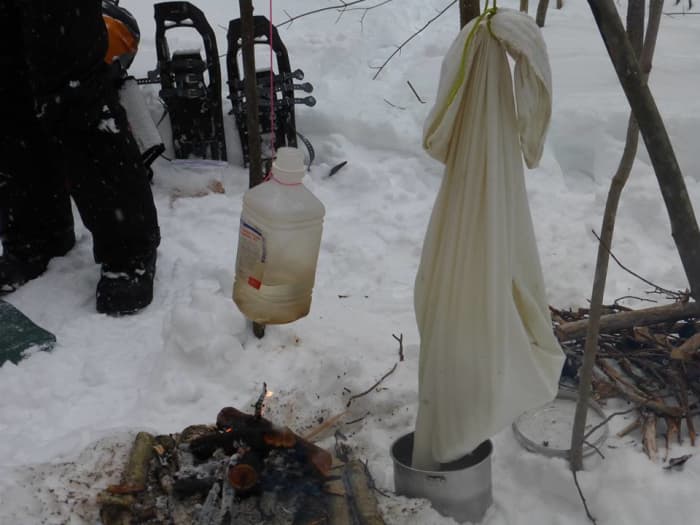 Melting snow over a fire in a pillowcase and boiling water inside a plastic bottle.