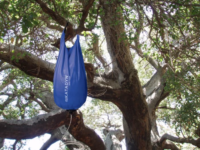 The gravity bag hangs from a tree branch, using the force of gravity to pull water through the filter.