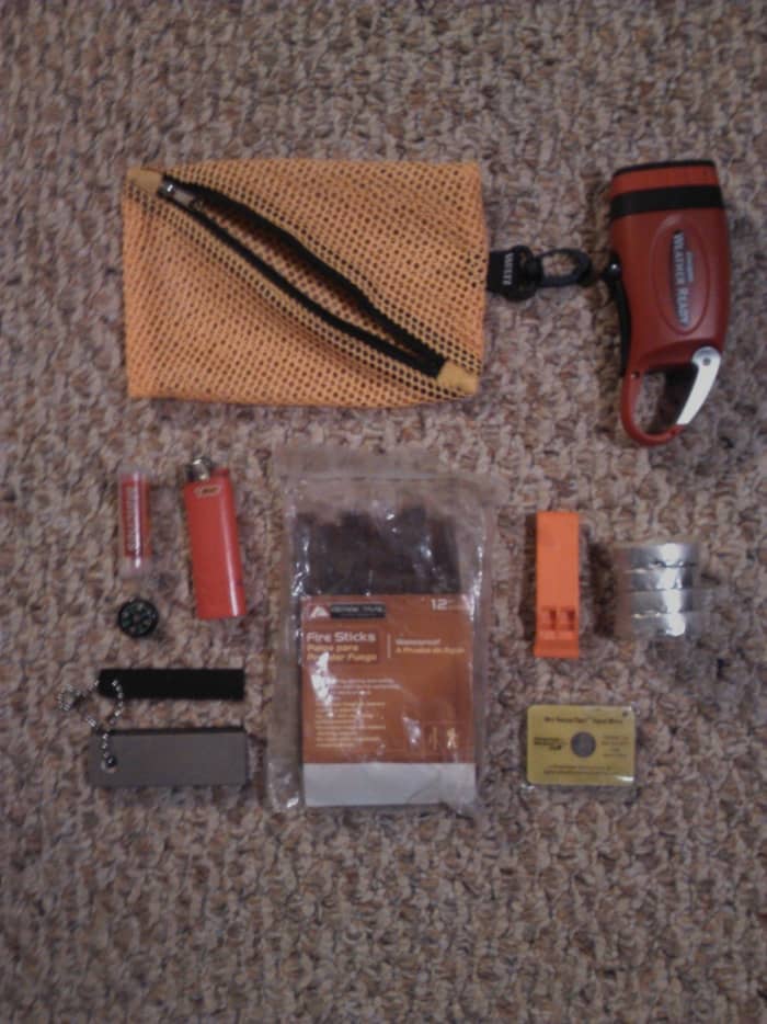 From left to right: crank flashlight, waterproof matches, lighter, flint with striker, fire sticks, whistle, tealights and signal mirror.