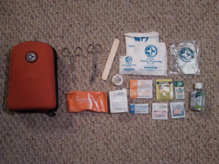 From left to right: first aid kit, surgical scissors, tongue depressor, sterile gauze, gloves, CPR mouth mask, itch and insect ointment, aspirin, sanitary wipes and hand sanitizer.