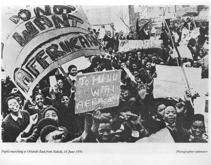 Students within the main body marching to the stadium and exuberantly showing placards which state how the students felt about the Afrikaans issue in 1976