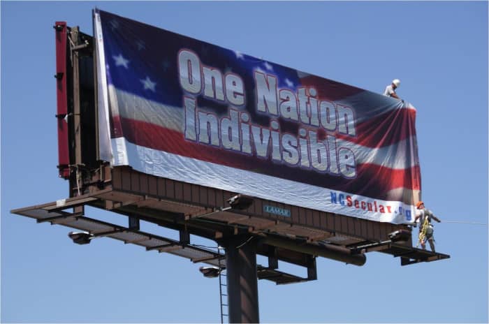 A billboard proclaims "One Nation Indivisible" against a backdrop of an American flag.