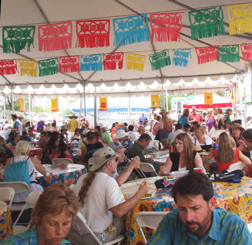 Attendees share an outdoor tent, while eating meals bought at ethnic food booths.