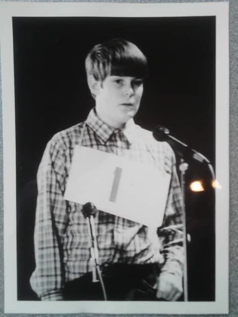 The author at 13, stepping up to the mic at the Spelling Bee. Hair by Weed Whacker, shirt by Krusty's Rodeo Clown Outlet.