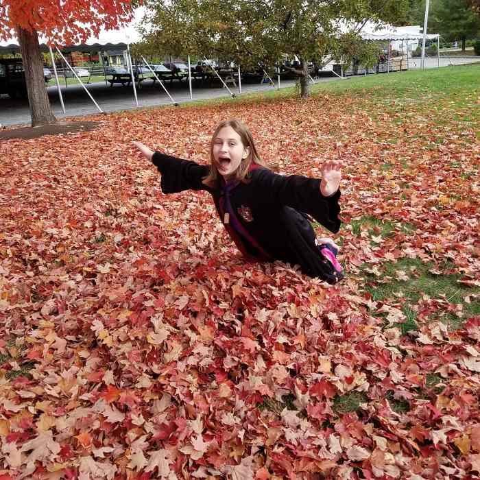 My daughter wearing a Harry Potter robe as she falls into a pile of leaves at the Ecotarium in Worcester, MA