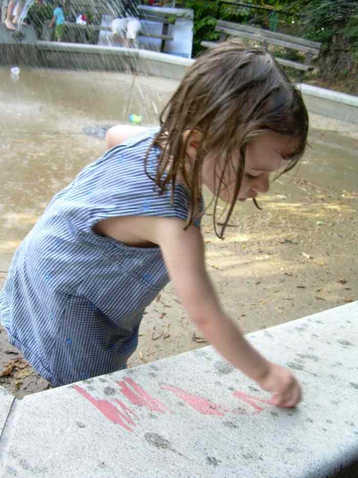 My young daughter drawing in chalk on the wall of a water fountain at our local park