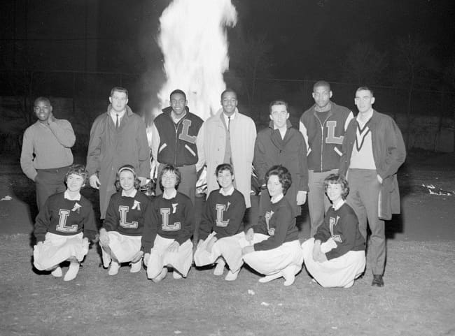 Players and cheerleaders celebrate the beginning of basketball season in front of a bonfire at Pow Wow Weekend, November 30, 1962.