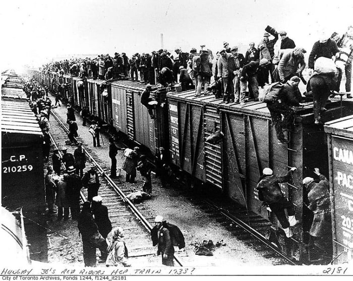 On to the next camp! Men board a freight train, including the roof, in order to find another work camp.