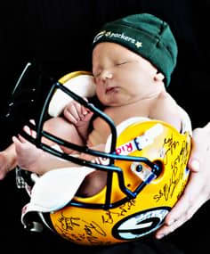 Sports Themed Gift Giving Ideas - photo of baby held in a Green Bay Packers helmet as a cradle wearing a Green Bay Packers bonnet