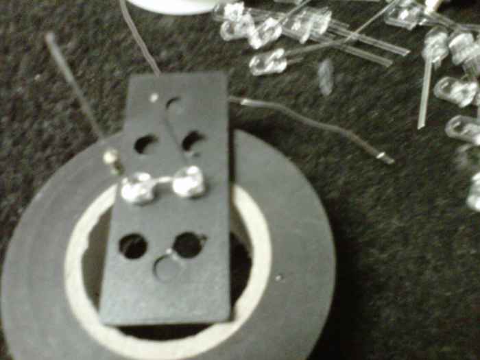 End of the box, drilled with a pair of LEDs ready to solder. You are soldering the - end of the one with the resistor to the + end of the other. Thus the pair's positive end has a resistor and negative end is just a lead.