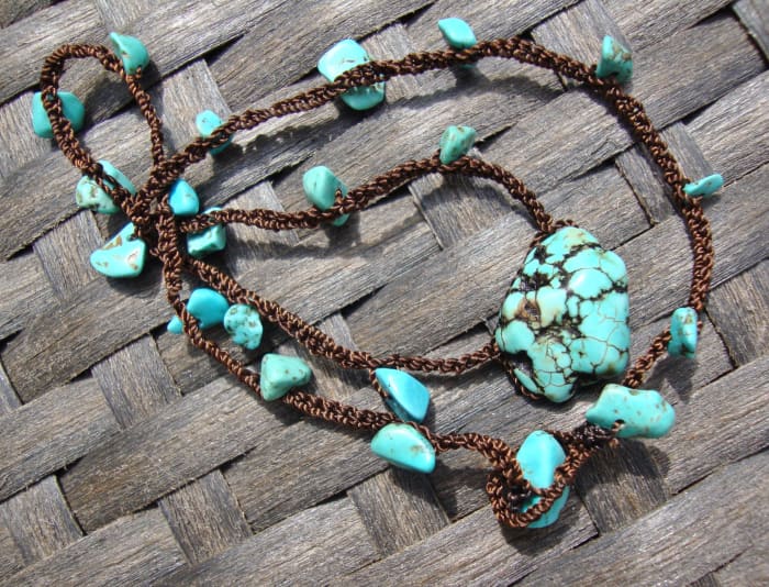 This is a tightly chained crocheted neclace with brown cording and turquoise nuggets. The clasp is a loop and a larger nugget goes into it.