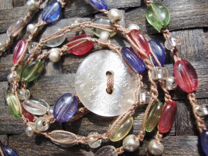 This crocheted necklace has larger glass beas and small silver glass beads. The shell button is used as the clasp and goes through a loop.