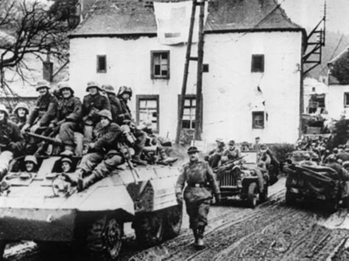 Germans troops moving west in captured American vehicles on Dec 16-17. In front is an M8 Greyhound and a jeep next in line. I believe this village to be Honsfeld.
