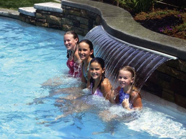four children in a swimming pool with fountain behind them massaging their necks and upper backs