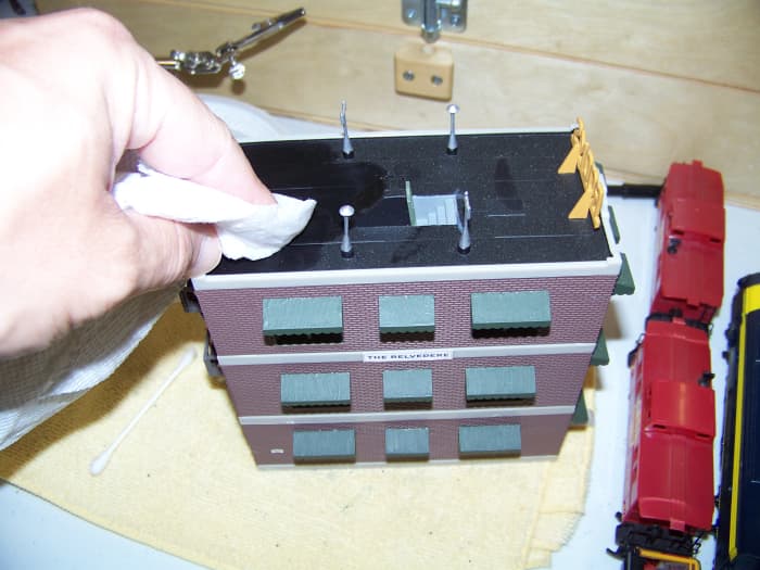 I use damp paper towels to clean buildings. Water does not seem to affect the dried acrylic paint I use.