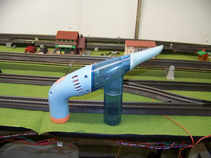 I use a small battery powered hand vacuum to remove debris from my layout. The nose of this vac is circular and small so it easily fits into small areas like between the rails.
