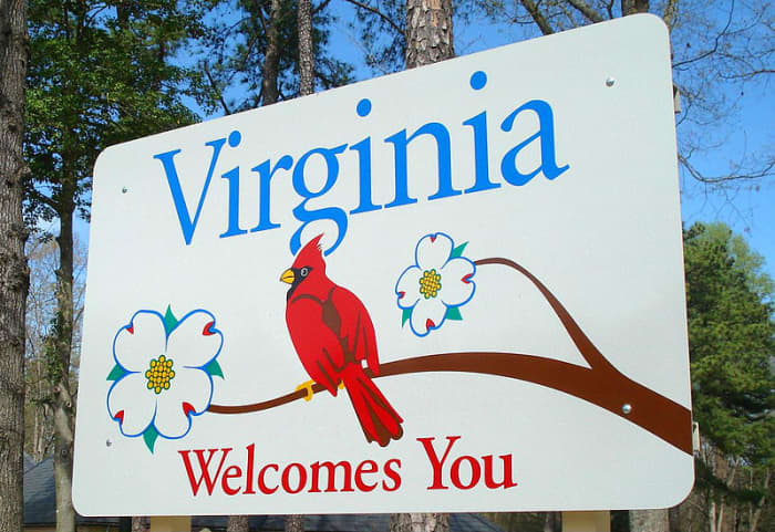This sign welcomes people to Virginia. It includes the cardinal which is the state bird, and the dogwood which is the state tree and flower.