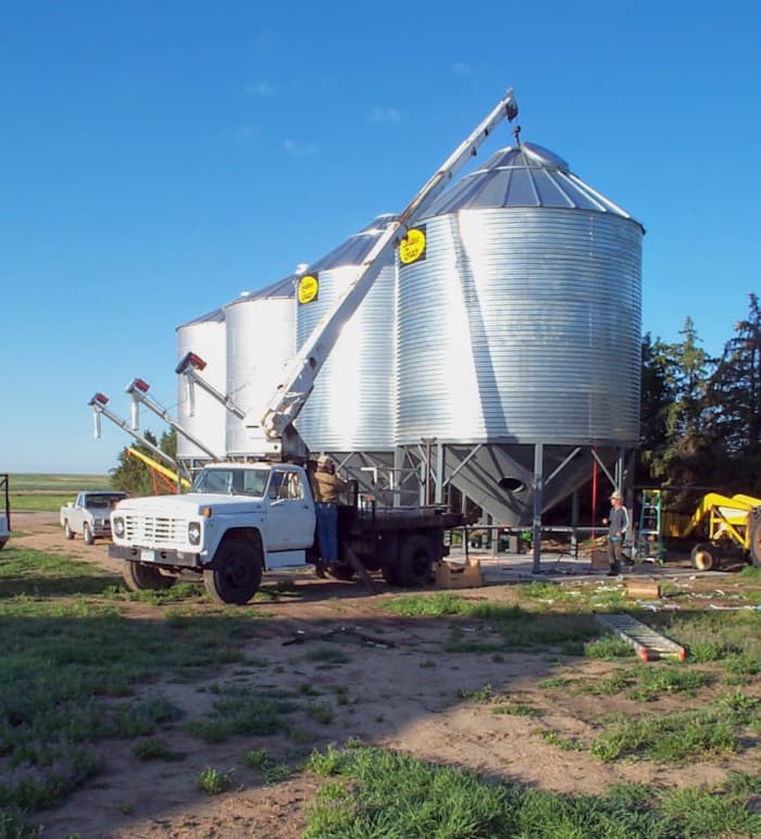 This skilled boom truck operator lifts this 4,000 bushel bin slowly in place while a ground crew helps guide it with ropes.