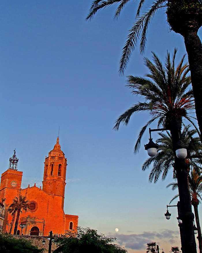 Sunset and moonrise over Iglesia de Sant Bartomeu i Santa Tecla, a 15th-century church in Sitges, Spain.
