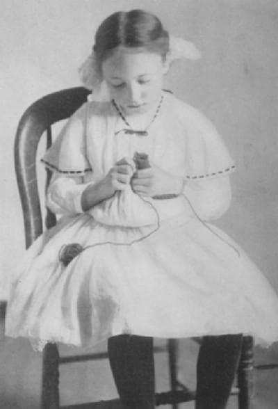 A young girl from the early 1900s knits with a knitting spool. From the book Spool Knitting by Mary A. McCormack