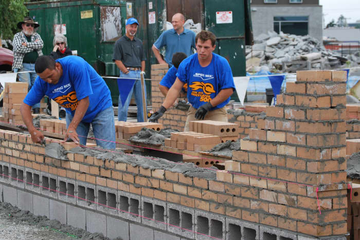 A small gang of bricklayers building a brick-wall overhand. This practice is not the best practice, it cannot be allowed everywhere, because when the building is tall it might become dangerous, but it is safe enough in this case.