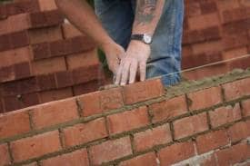 A bricklayer laying bricks on a single wall in stretcher bond. Note how the mortar has been spread and trimmed back and how he lays his bricks following his line.