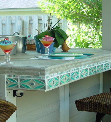 beautiful blue, teal and aqua tile edge an outdoor built in table complete with table setting and tropical drinks