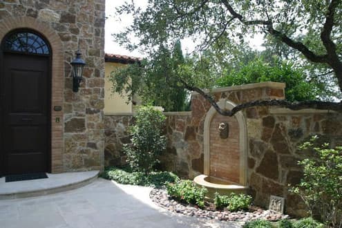 a wall decorated with a lion head and arched tile surround accent the water fountain in this beautiful garden courtyard with walled stone fence