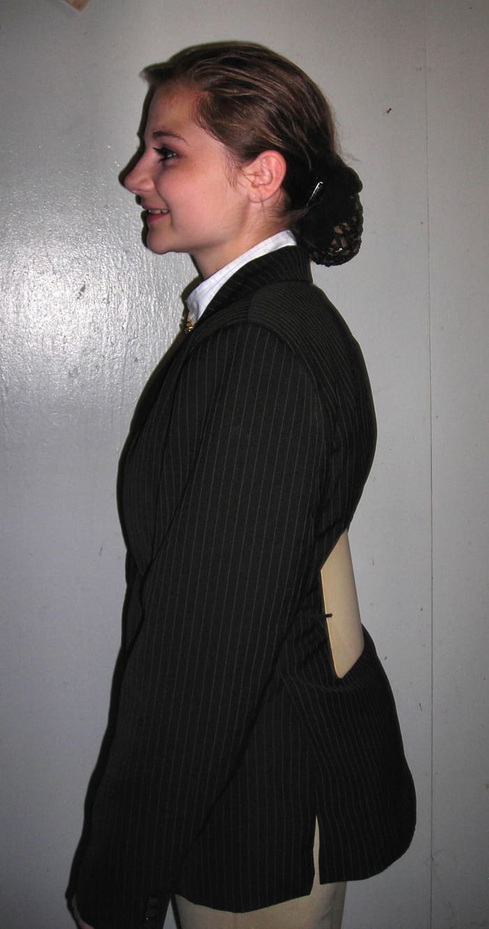 Not so perfect -- Tied too snug. Coat is puckering and the number is already starting to tuck down into the waistline of her breeches.