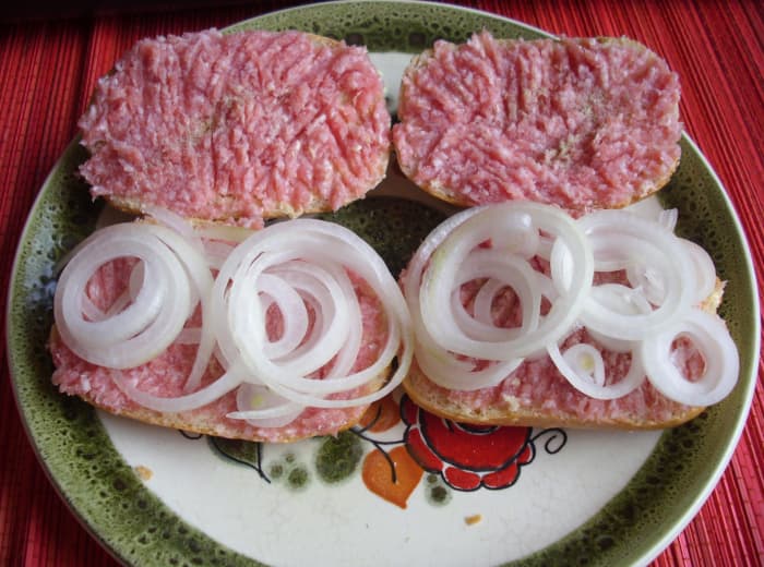 Ready to eat half wheat bread rolls spread with margarine, raw minced pork, salt, pepper and with or without sliced onions.