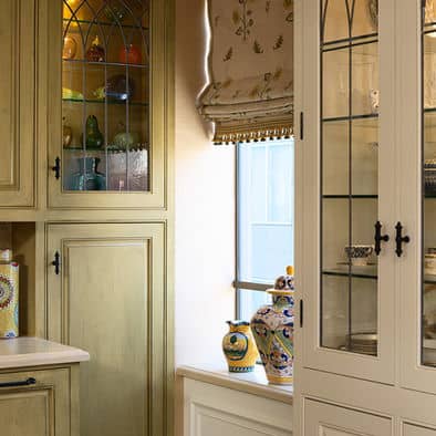 High quality brass knobs combined with glass cabinets add an Old World touch to the sage green and white cabinets