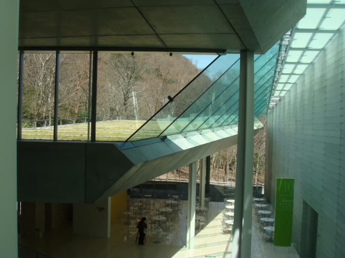 Photo taken from the ground level, captures one floor down featuring the cafe, and the roof of the structure, all grassy, is clearly visible through the glass.